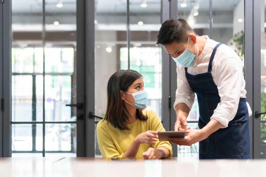 Asian Waiter wearing protective face mask taking order from Female customer on digital tablet in modern cafe Asian Waiter wearing protective face mask taking order from Female customer on digital tablet in modern cafe
