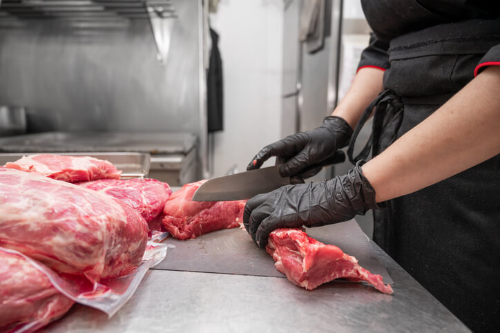 Butcher using a knife to slice cuts of red meat.