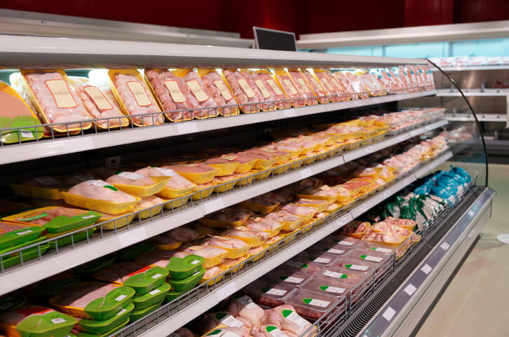 Pre-packaged meats on retail grocery store cooling shelves.