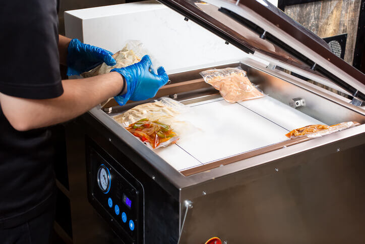 Food worker using a vacuum sealer to prevent freezer burn.