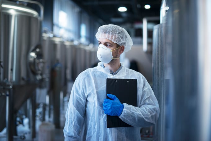 Technologist in protective white suit with hairnet and mask standing
