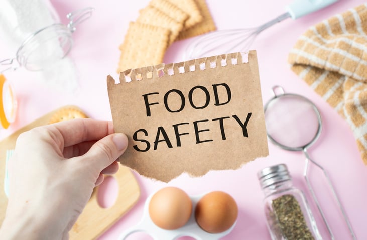 The girl holds a card with the text FOOD SAFETY