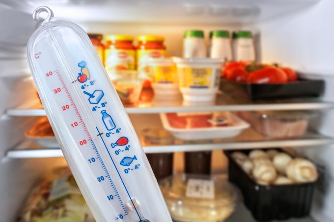 Thermometer in front of open fridge refrigerator filled with food in kitchen
