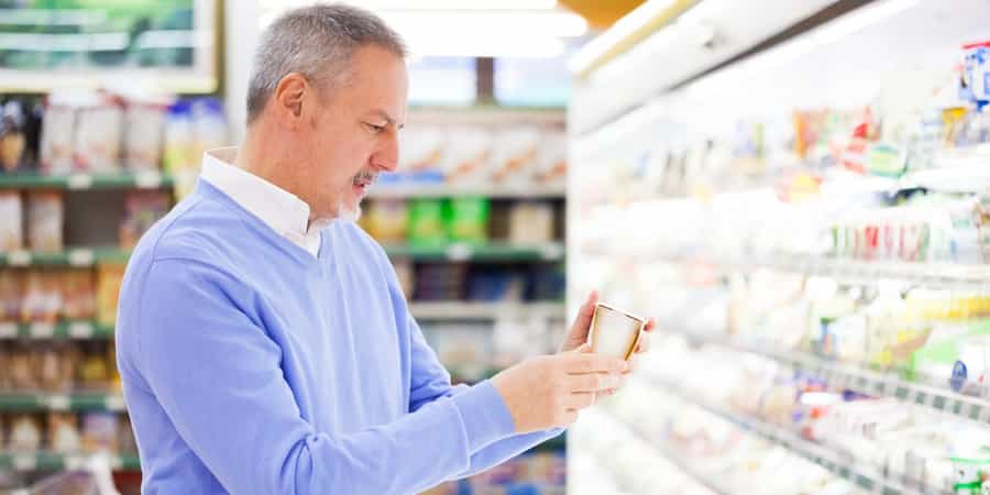 Man reading the expiration date on a product in a grocery store aisle. Man reading the expiration date on a product in a grocery store aisle.