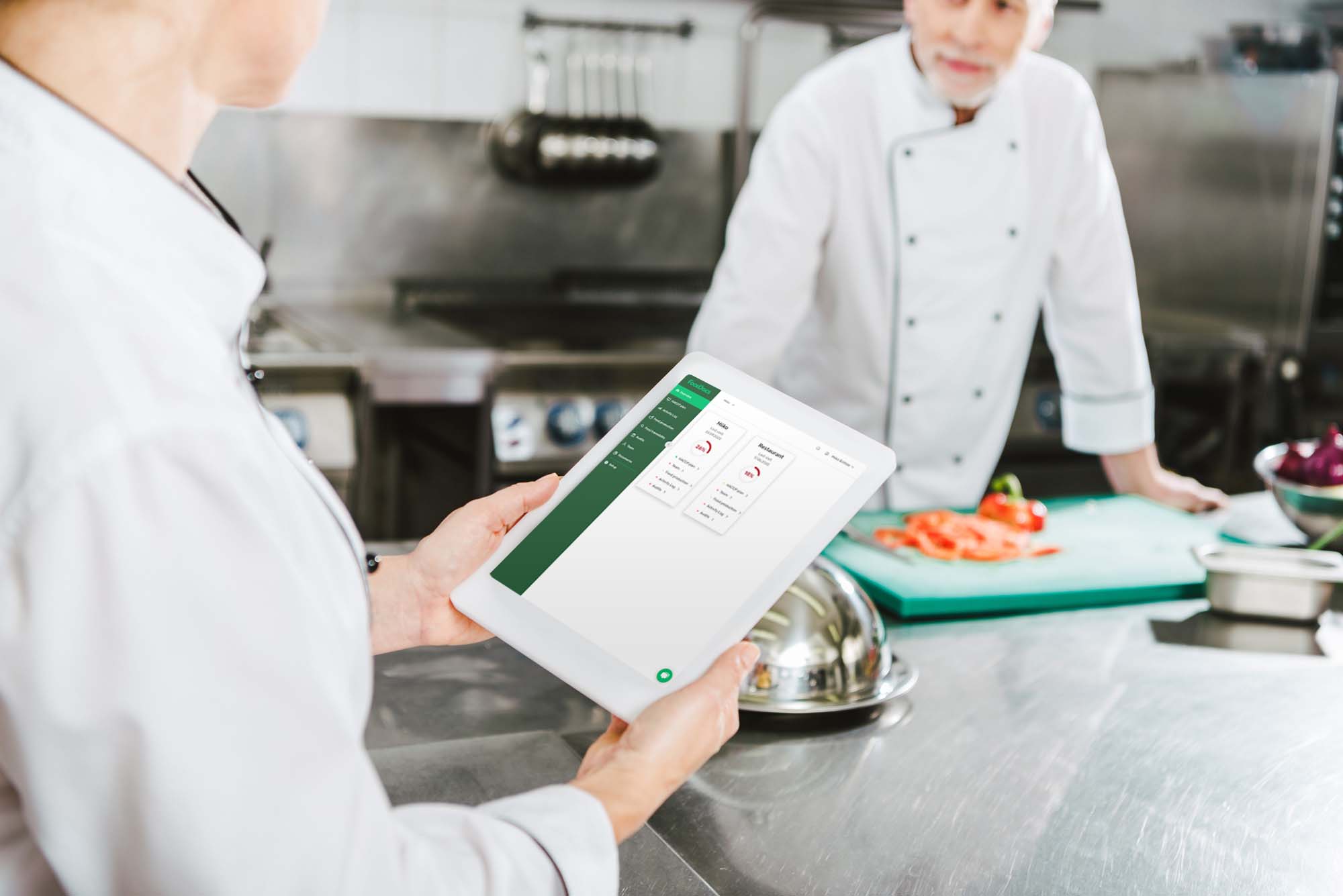 Kitchen staff looking at the real-time dashboard inside of FoodDocs' food safety compliance software on a tablet.